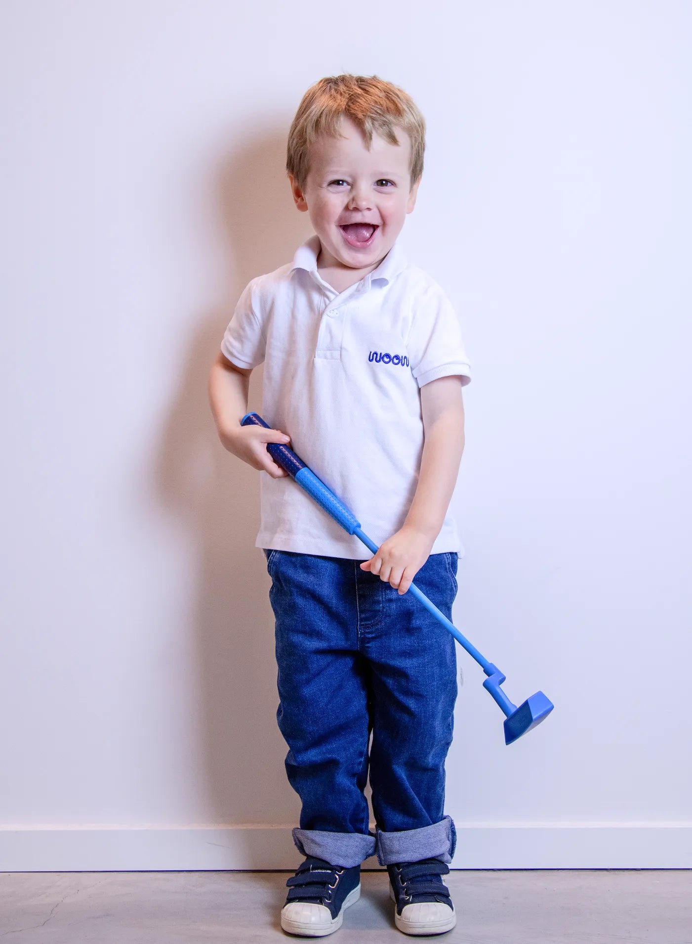 Child wearing a white polo shirt with a logo, holding a blue golf club against a plain background
