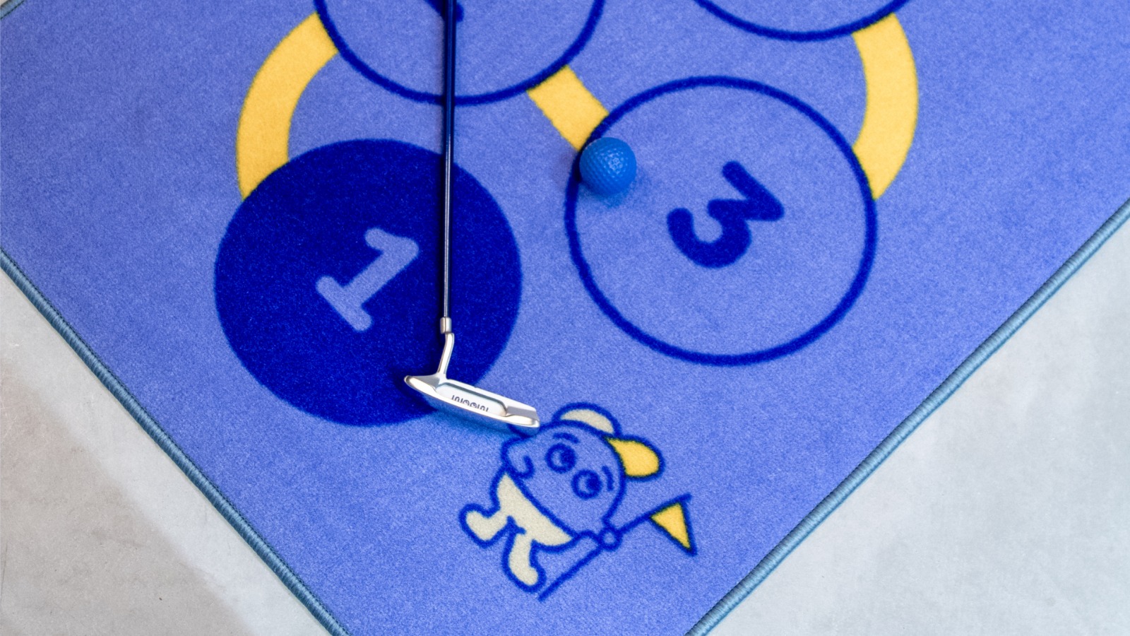 Ein kleines Kind spielt zu Hause Golf auf einer WOOW Golf Putting-Matte, während ein Elternteil zusieht