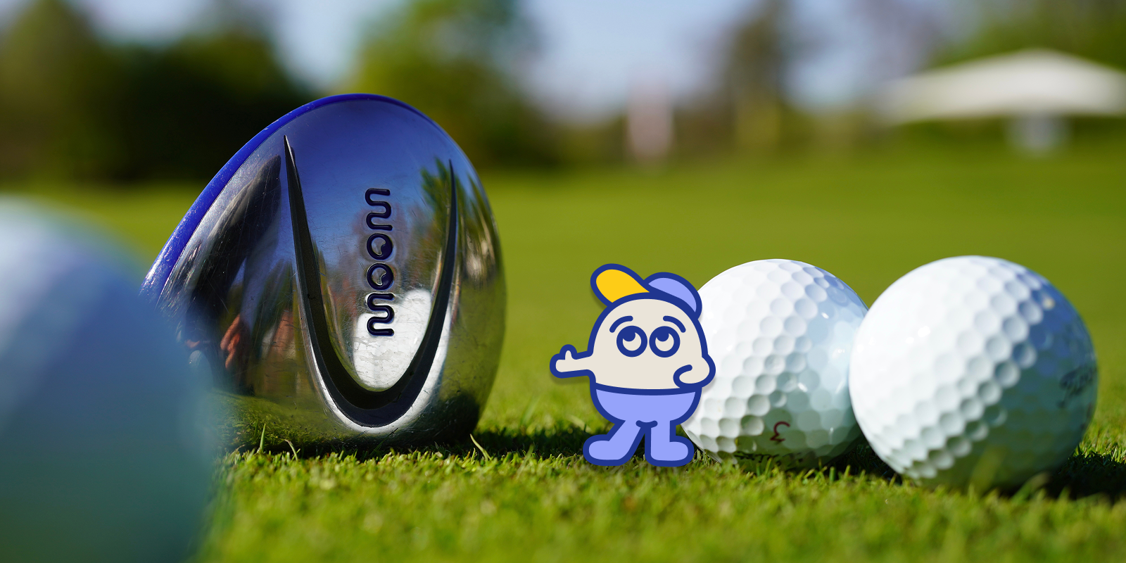 Ein WOOW Golfschlägerkopf für Kinder neben Golfbällen und dem Maskottchen Archie auf Gras
