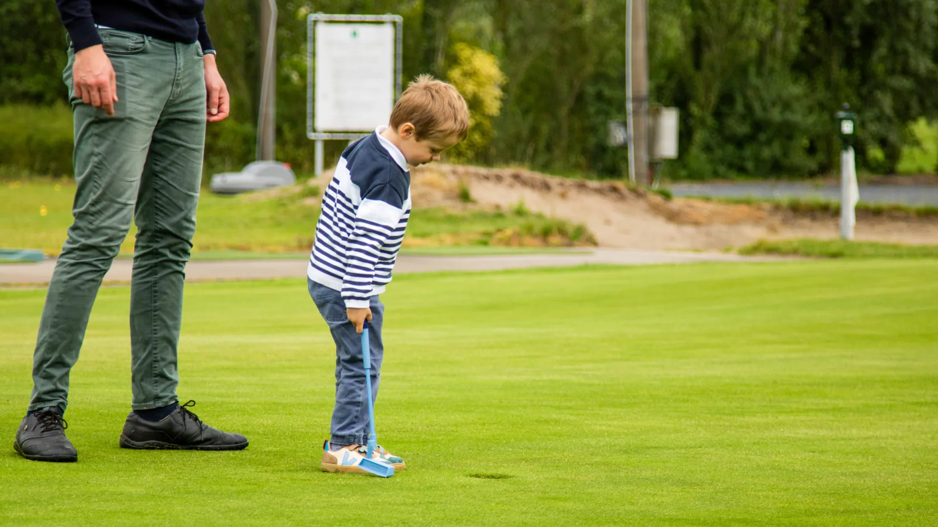 A young child putting on a green with a light blue WOOW putter while a parent watches
